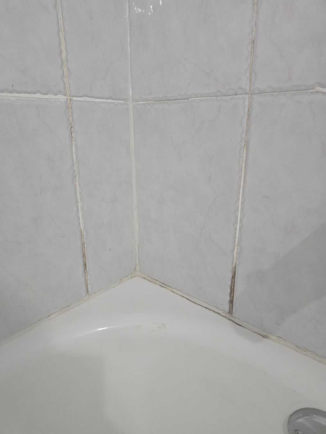 Before: dark, failing caulk in the corner where the tub meets the wall